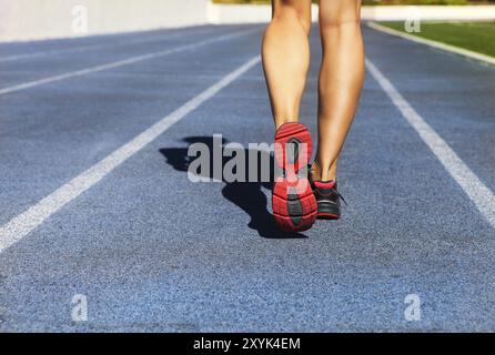 Atleta runner a piedi lungo la pista dello stadio. Primo piano su scarpe e gambe femminili. Allenamento fitness estivo femminile. Jogging, sport, stile di vita sano e attivo concep Foto Stock