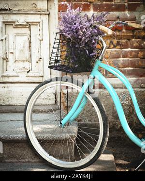 Vintage bicicletta atto con cesto con fiori di lavanda vicino alla vecchia porta di legno Foto Stock