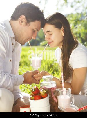 Giovane coppia felice in amore bere latte shake al picnic a molla nella giornata di primavera. Ritratto all'aperto Foto Stock