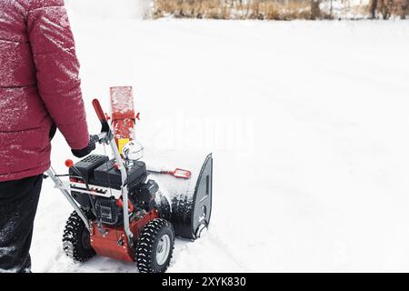 Particolare della soffiatrice portatile di neve rossa alimentata a benzina in azione. Uomo all'aperto che usa una macchina spazzaneve dopo la tempesta di neve. Rimozione neve, lanciatore assestan Foto Stock