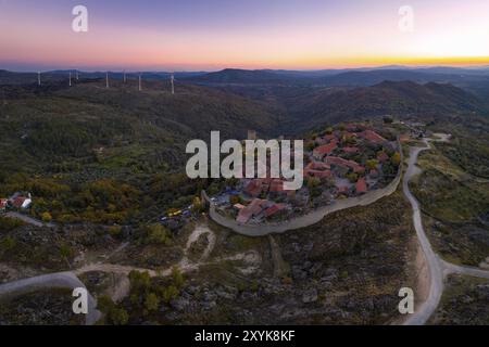 Panorama aereo del drone Sortelha storico villaggio al tramonto con luci sul castello eolico turbine eoliche e paesaggio naturale, in Portogallo Foto Stock