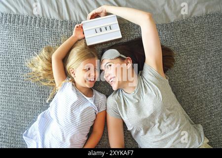 Tenetevi stretti. Una donna emotiva e carina che abbraccia la figlia stretta mentre passa la mattina a letto e si sente felice. Naso a naso. Regge Foto Stock