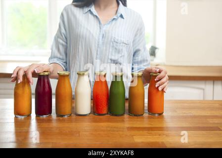 Nutrizione dietetica con succo disintossicante. Donna sana che posa con bottiglie di succo fresco di frullato disintossicante. Primo piano di una bella ragazza in forma felice in cucina Foto Stock