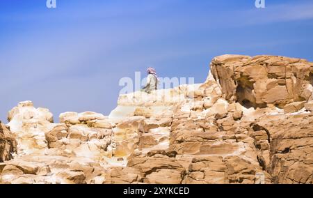 Bedouin seduto sul picco di una alta roccia di pietra contro un cielo blu in Egitto Dahab Foto Stock