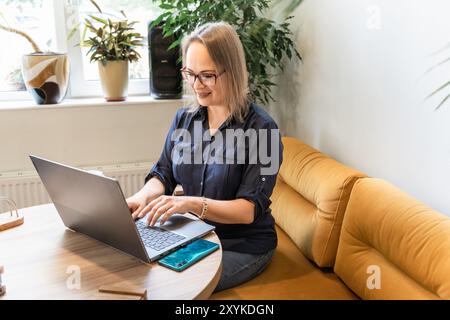 Donna d'affari sorridente che lavora al computer portatile mentre si siede sul divano nel bar Foto Stock