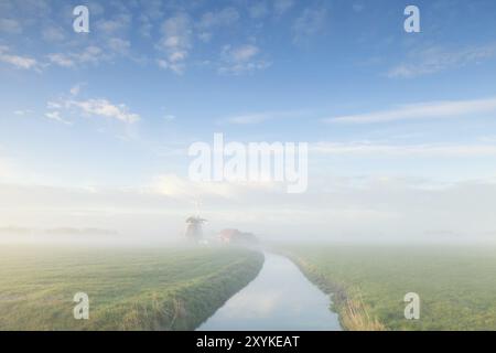 Affascinante mulino a vento lungo il fiume nella mattina nebbiosa, Paesi Bassi Foto Stock