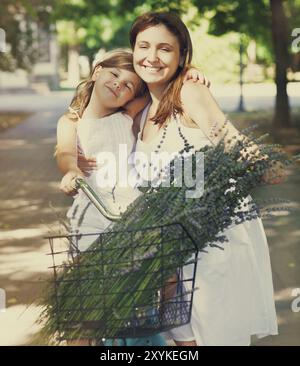 Bella e felice giovane donna sulla bicicletta con sua figlia. Entrambi sorridenti, d'estate il parco in background Foto Stock