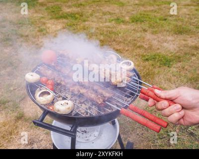 Primo piano di uno chef girando gli spiedini di carne sul barbecue a caldo Foto Stock