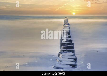 Groynes che sporge all'orizzonte nel Mar Baltico. Lunga esposizione con colori silenziati. Paesaggio girato dal mare Foto Stock