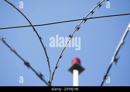 Filo spinato e luce di emergenza rossa sfocata sullo sfondo contro il cielo blu, messa a fuoco selezionata, profondità di campo ridotta Foto Stock