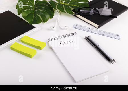 Tavolo da ufficio bianco moderno con tablet, occhiali, penna, matita, righello, pianta monstera, blocco note e tazza greca di caffè. Vista dall'alto, lastre piatte cimasa Foto Stock