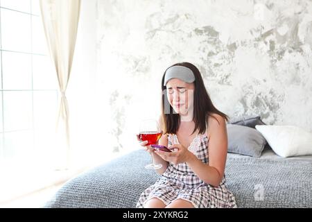 Donna che piange a casa dopo la rottura con il suo fidanzato. Tenendo lo smartphone e bere vino rosato Foto Stock