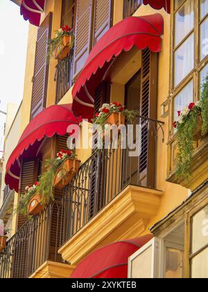 Casa vivace con tende rosse e fiori fioriti in balconi, irradia un'atmosfera calda e accogliente, tipico stile mediterraneo, palma de Majorc Foto Stock