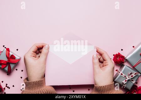 Le mani femminili tengono lettera d'amore vuoto messaggio in busta aperta, biglietto di auguri di San Valentino o invito bianco mock up. Spazio di copia, vista dall'alto. Rosa ba Foto Stock