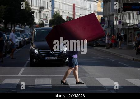 Vienna, Austria. 29 agosto 2024. AUSTRIA; VIENNA; 20240829; Un uomo porta un piccolo divano dall'altra parte della strada a Vienna il 29 agosto 2024. // Österreich; WIEN; 20240829; Ein Mann trägt ein kleines Sofa über eine Strasse in Wien am 29. Agosto 2024. - 20240829 PD23359 credito: APA-PictureDesk/Alamy Live News Foto Stock