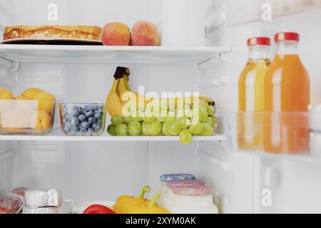 Vista frontale del frigorifero a due porte aperto o della porta del frigorifero riempito con frutta fresca, verdura, succo di frutta, pieno di cibi sani e ingredienti all'interno Foto Stock