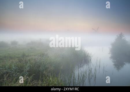 Mulino a vento e fiume nella nebbia mattutina, alba estiva nei Paesi Bassi Foto Stock