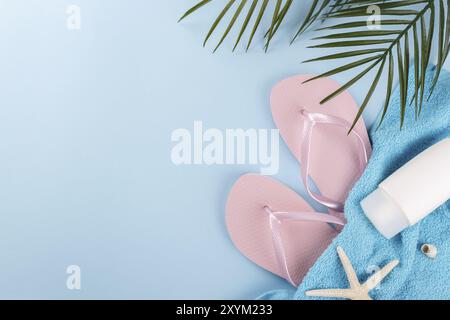 Vacanze estive, pantofole da spiaggia rosa, infradito, asciugamano, ramo di palma, crema e conchiglie di mare su sfondo blu Foto Stock