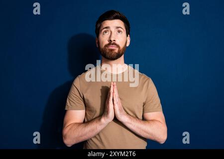 Foto di un uomo gentile con un'elegante t-shirt beige con barba che tiene le braccia insieme Guarda lo spazio vuoto isolato su sfondo blu scuro Foto Stock