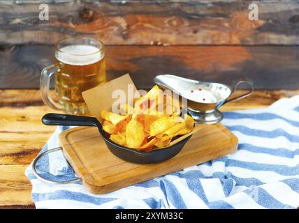 Patate fritte in padella con la salsa di aglio e una birra su di un tavolo di legno Foto Stock