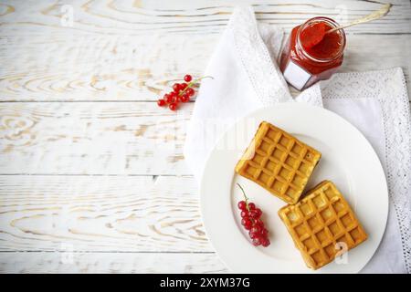 Le cialde con il rosso confettura di ribes e mirtilli su una piastra bianca su sfondo di legno Foto Stock