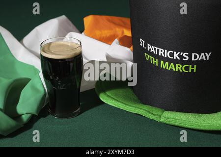 St Patrick giornata con una pinta di birra nera, cappello e bandiera irlandese su un tavolo verde Foto Stock