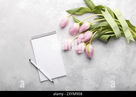 Aprire il blocco note di vuoto e di profumo di rosa fiori di tulipani su grigio tavolo in pietra vista superiore nel piatto stile di laici. Femmina desk top Foto Stock