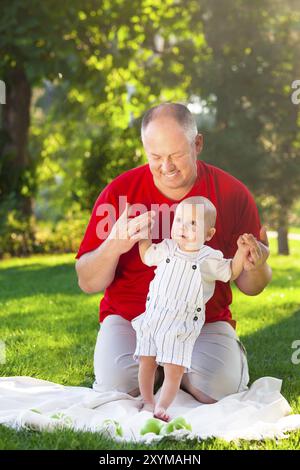 Il bambino ad imparare a camminare all'esterno. Padre Felice e suo figlio giocare nel parco insieme. Outdoor ritratto di famiglia felice Foto Stock