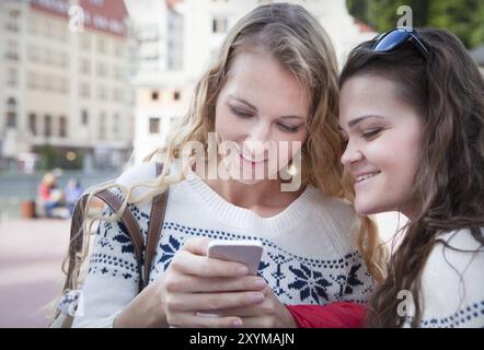 Due amiche donne felici che condividono i social media in uno smartphone all'aperto in città. Due giovani donne che guardano insieme il telefono cellulare mentre si distinguono Foto Stock