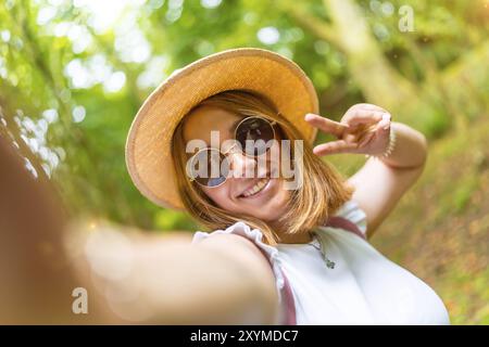 Punto di vista personale di una giovane donna caucasica bella che gestiva il successo con le dita mentre si fa un selfie nella foresta Foto Stock