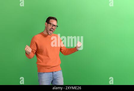Giovane uomo d'affari con gli occhi chiusi che urla ecstaticamente e che scuote pugni su sfondo verde Foto Stock