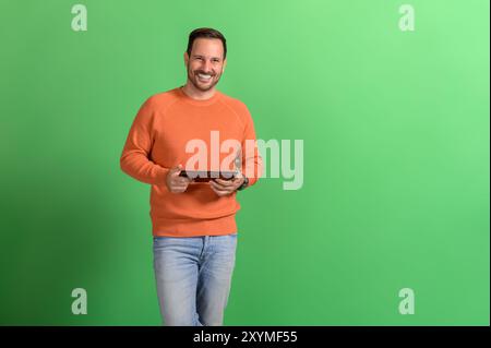 Ritratto di un bellissimo professionista sorridente che controlla le e-mail su un tablet digitale su sfondo verde Foto Stock