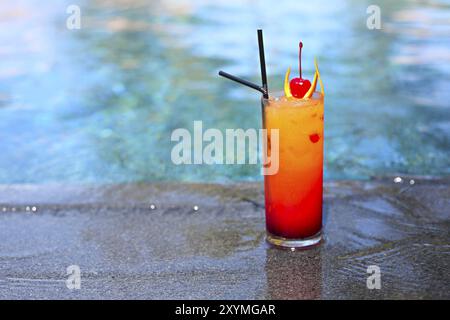 Vetro con un luminoso tequila sunrise cocktail in piscina. Resort di lusso sull'isola tropicale Foto Stock