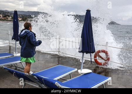 Le onde si infrangono contro il molo di un molo sul quale si trova una donna, Diana Marina, Italia, 18/08/2024, Diano Marina, Liguria, Italia, Europa Foto Stock