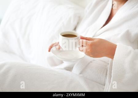 Donna che indossa bianco accappatoio con tazza di caffè nelle sue mani. Close up Foto Stock