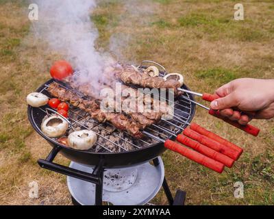 Primo piano di uno chef girando gli spiedini di carne sul barbecue a caldo Foto Stock