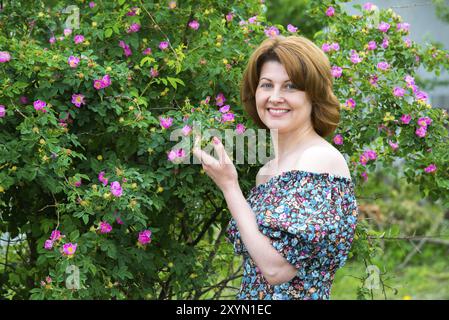 Donna sorridente in piedi vicino a una rosa di cane in fiore Foto Stock