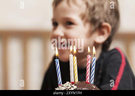 Poco sorridente ragazzo bambino soffiando celebrazione di compleanno torta dolce candela fire Foto Stock