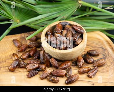 Datteri in una ciotola di legno con foglie di palma Foto Stock