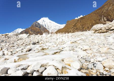 Gelido fiume alpino in esecuzione attraverso white terreno roccioso paesaggio ad alta quota tundra alpina con Langtang Lirung sfondo picco vicino Kyanjin Gompa Foto Stock