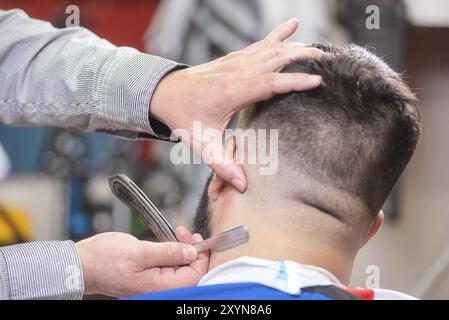 Le mani del barbiere si chiudono, la testina di rasatura di un uomo barbuto Foto Stock