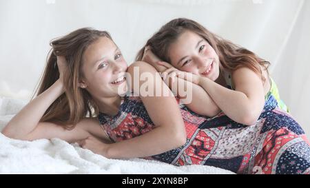 ritratto di due bambine felici sdraiate in una coperta bianca che ridono e scherza sullo sfondo chiaro Foto Stock