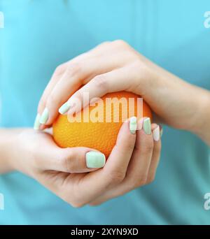 Le belle mani di una donna con il turchese french manicure holding arancione Foto Stock