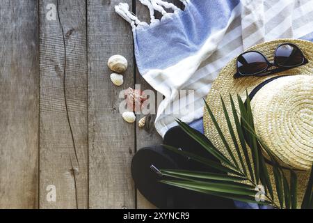 Concetto di viaggio, vacanza o fine settimana. Cappello di paglia con foglie di palma, scarpe e occhiali da vista, asciugamano su fondo in legno. Tempo di relax. Foto Stock