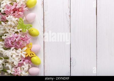 Sfondo pasquale con uova colorate, fiori di Giacinto e farfalle su sfondo bianco in legno Foto Stock