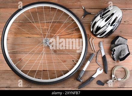 Vista dall'alto dell'attrezzatura da bicicletta disposta su un pavimento rustico in legno. Gli elementi includono: Ruota, pompa, guanti, utensili, casco e lucchetto. Formato orizzontale. Foto Stock