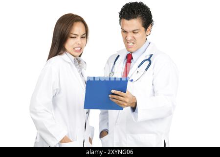 Un team di medici diversi uomini, donne, ispanici, asiatici che esaminano le cartelle mediche insieme grimacing con scioccato, reazione dolorosa, inorridito a Bad di Foto Stock