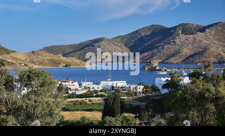 Vista di una baia e di una pittoresca cittadina costiera circondata da montagne e vegetazione verde sotto un cielo limpido, del porto di Grikos, di Grikos, di Patmos e dei dodecani Foto Stock