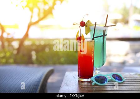 Vetro con un luminoso laguna blu e Tequila Sunrise cocktails presso la piscina. Resort di lusso sull'isola tropicale Foto Stock