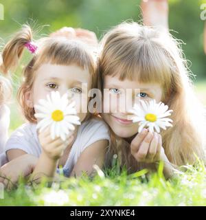 Bambini felici con fiori che lievitano sull'erba su sfondo verde primaverile Foto Stock